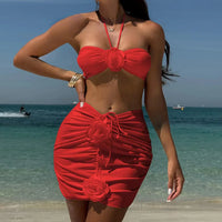 Maillot de bain trois pièces jupe fleurs en relief rouge porté de face sur la plage, bras relevé, fleurs sur la jupe froncée