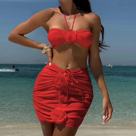 Maillot de bain trois pièces jupe fleurs en relief rouge porté de face sur la plage, bras relevé, fleurs sur la jupe froncée