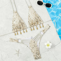 Bikini brésilien à sequins tour de cou beige posé à plat sur du marbre, haut à franges de coquillages et bas pailleté