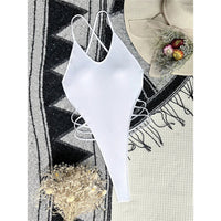 Maillot de bain une pièce blanc posé à plat sur un tapis gris et noir, avec lanières latérales croisées