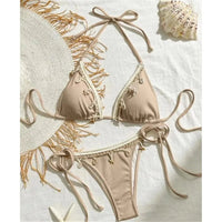 Bikini brésilien tour de cou patchwork à lanières marron clair posé à plat sur fond blanc, bordure crème et breloques