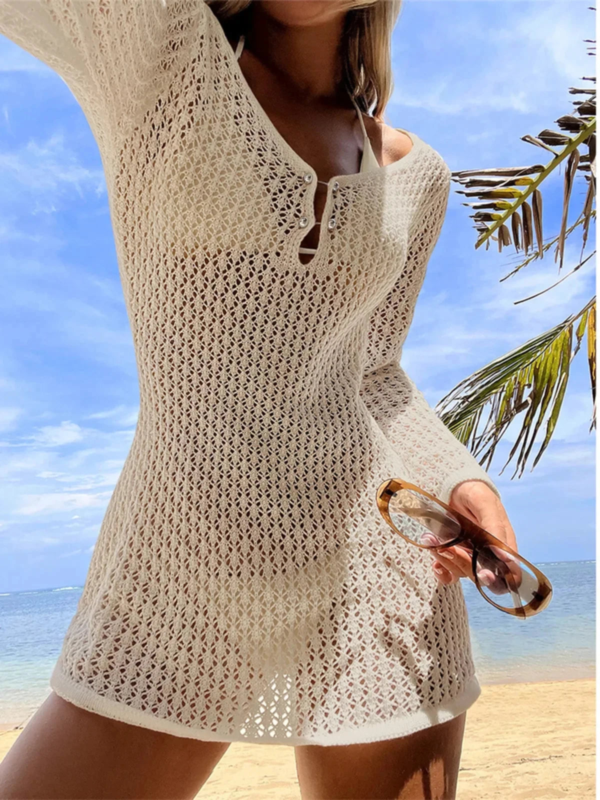 Tunique de plage en crochet à col V et manches longues beige, portée sur le sable avec des lunettes de soleil à la main