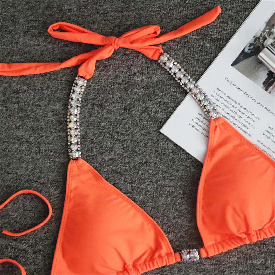 Gros plan sur le haut triangle orange à bretelles ornées de strass, nouée derrière le cou sur fond gris