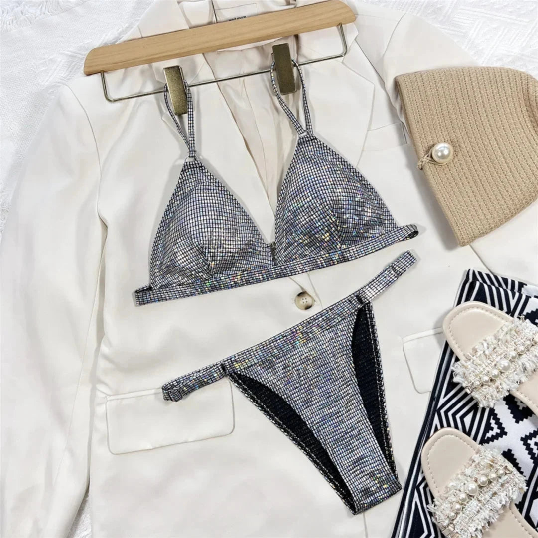 Bikini à paillettes argenté bas échancré posé à plat sur une veste blanche, bretelles chaînettes et sandales autour