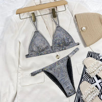 Bikini à paillettes argenté bas échancré posé à plat sur une veste blanche, bretelles chaînettes et sandales autour