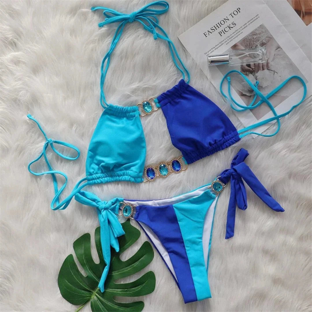 Bikini strass patchwork bleu posé à plat sur une fourrure blanche, haut bleu et bleu clair avec anneaux brillants et liens noués