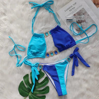 Bikini strass patchwork bleu posé à plat sur une fourrure blanche, haut bleu et bleu clair avec anneaux brillants et liens noués