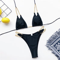 Bikini tour de cou à chaîne métallique noir posé à plat, chaînes dorées sur la culotte, à côté d'un citron et d'un tapis