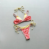 Bikini à carreaux rouge et blanc posé à plat sur fond gris, liens jaune pâle à nouer et doublure jaune sur le haut