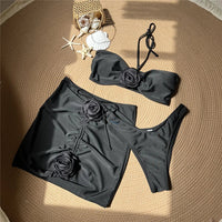 Maillot de bain trois pièces jupe fleurs en relief noir à plat sur un tapis rond, avec coquillages et étoiles de mer