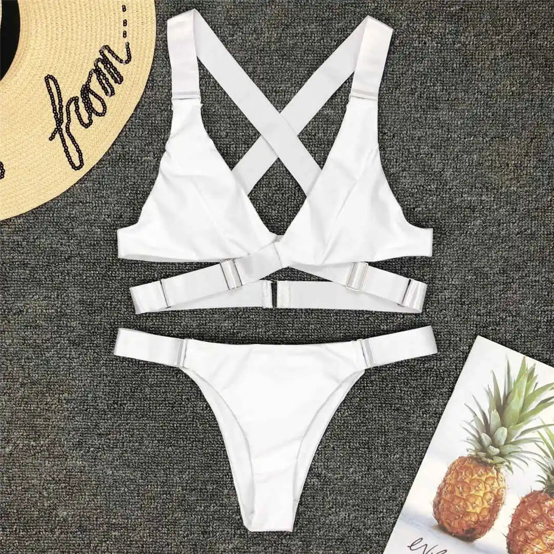 Bikini sans armatures croisé dans le dos blanc posé à plat sur un tapis gris, bretelles croisées et anneau central