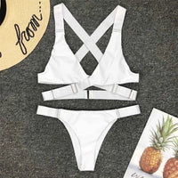 Bikini sans armatures croisé dans le dos blanc posé à plat sur un tapis gris, bretelles croisées et anneau central