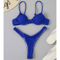 Bikini triangle à armatures côtelé échancré bleu roi posé à plat sur fond gris, tongs blanches à côté