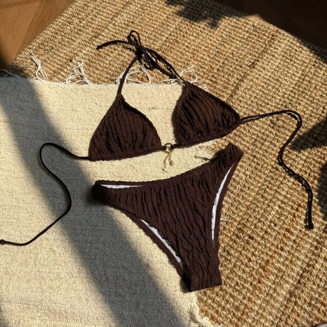 Bikini brésilien tour de cou effet froissé marron à plat sur un tapis en osier, lacets longs et pendentif doré