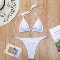 Bikini mini strass sans armatures taille basse blanc posé à plat sur bois, strass et anneaux sur le haut et la culotte