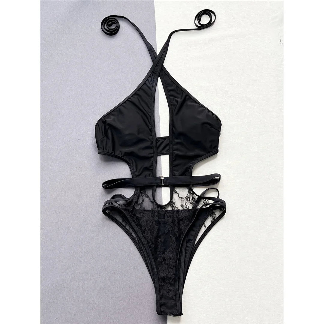 Maillot une pièce noir à col tour de cou, découpe en V au décolleté et partie basse en dentelle, posé à plat sur fond gris et blanc