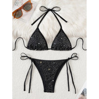 Bikini à paillettes col halter échancré taille basse noir à plat sur une fourrure blanche, paillettes visibles