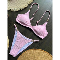 Bikini triangle rose décolleté en V strassé posé à plat sur une table en bois, bretelles fines et anneaux dorés