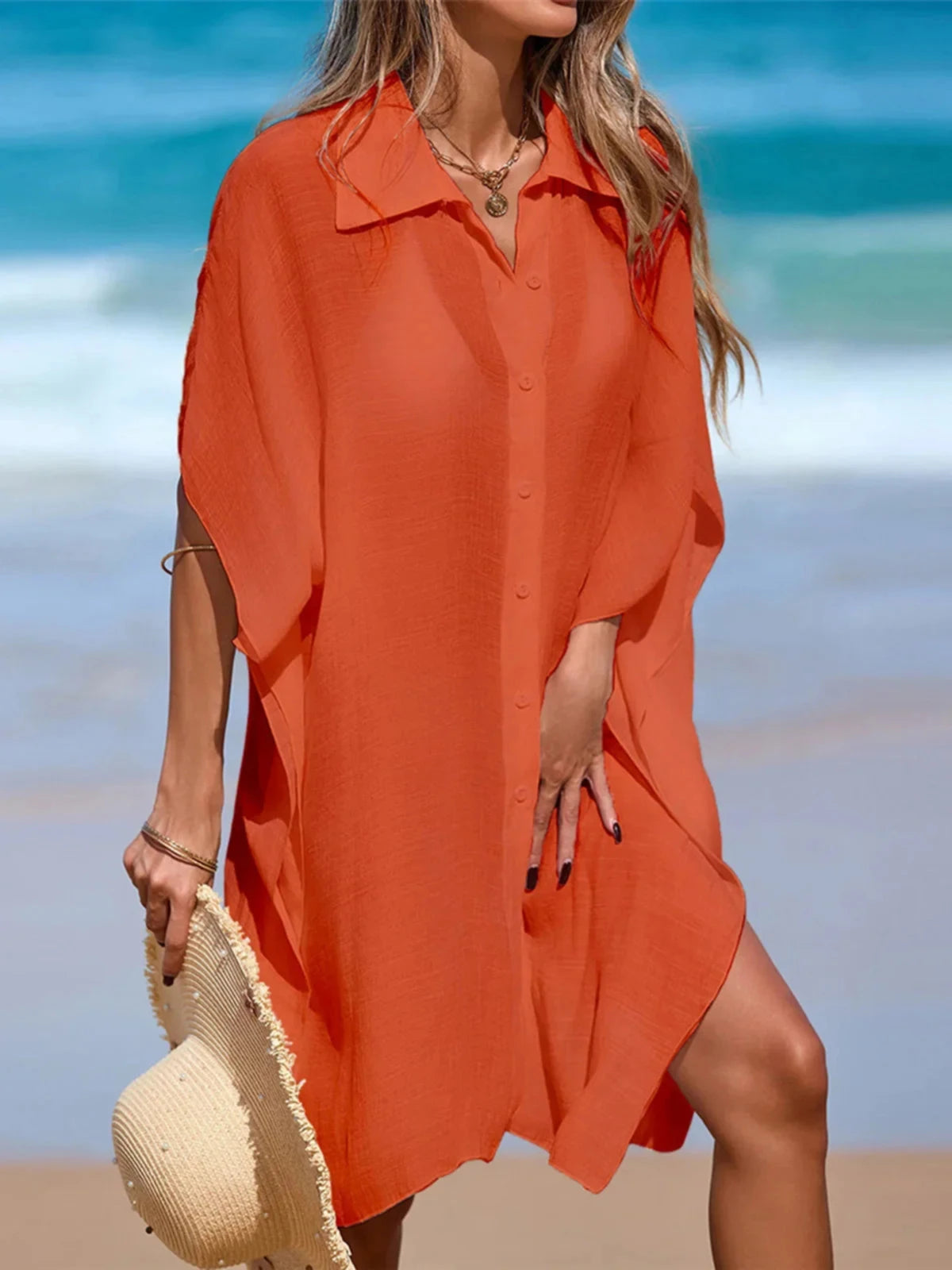 Chemise de plage longue à manches courtes en maille orange portée de face, chapeau de paille au bras et boutons devant