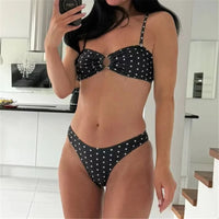 Bikini bandeau à anneau brésilien noir à pois blancs porté de face dans une pièce blanche, haut bandeau à anneau central