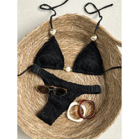 Bikini tour de cou effet froissé noir posé à plat sur un panier en osier, liens fins et perle nacrée au centre du triangle