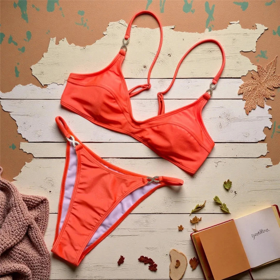 Bikini triangle orange posé à plat sur bois peint, plaid rosé et carnet au premier plan, bas à petits anneaux strassés
