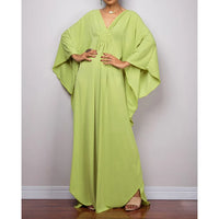 Robe de plage longue kaftan manches chauve-souris vert anis portée de face avec sandales beiges aux pieds, ourlet asymétrique