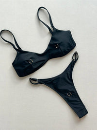 Bikini string micro triangle à anneaux métalliques noir posé à plat sur fond clair, anneaux ronds sur le haut et le bas