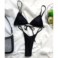 Bikini triangle string mini rembourré taille basse noir à plat sur un drap blanc, anneaux en forme de cœur