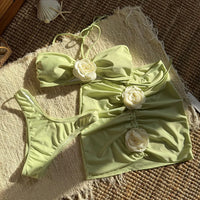 Maillot de bain trois pièces jupe fleurs en relief vert pistache à plat sur un tapis, avec fleurs blanches en relief
