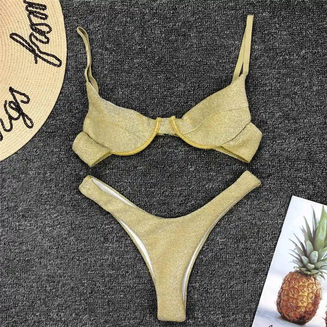 Bikini jaune pailleté à armatures posé à plat sur un tapis gris, à côté d'un chapeau de paille brodé