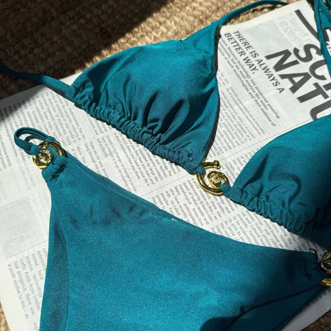 Gros plan sur le haut bleu paon du bikini tour de cou à anneau métallique, bonnet froncé et anneau doré sur le côté