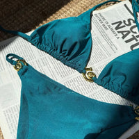 Gros plan sur le haut bleu paon du bikini tour de cou à anneau métallique, bonnet froncé et anneau doré sur le côté