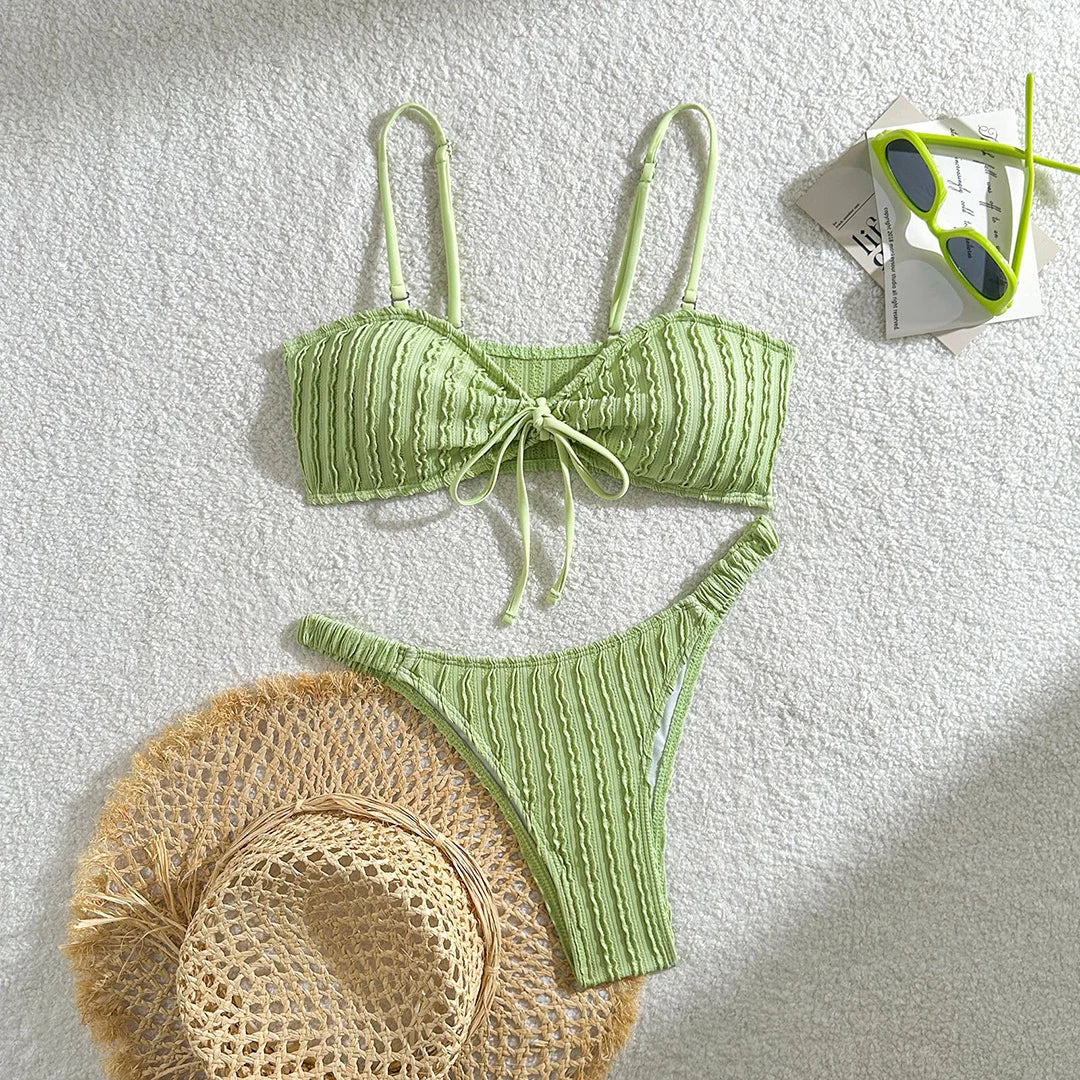 Bikini brésilien texturé froissé à nœuds vert clair posé à plat avec un chapeau en paille et des lunettes vertes