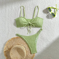 Bikini brésilien texturé froissé à nœuds vert clair posé à plat avec un chapeau en paille et des lunettes vertes