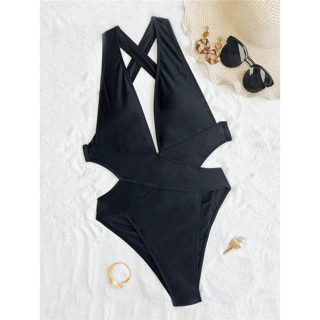 Maillot une pièce noir posé à plat sur tapis blanc, découpe croisée sur les hanches, avec lunettes et chapeau