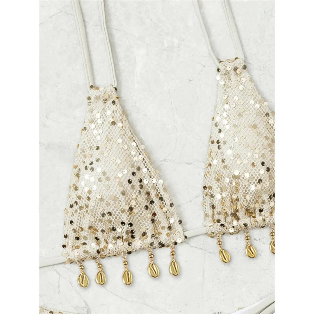 Gros plan sur le haut à sequins beige orné de petites coquilles dorées en franges qui pendent sous les triangles