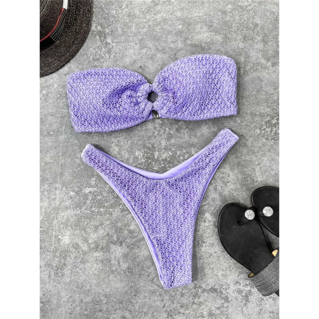 Bikini bandeau échancré violet texturé posé à plat sur du béton gris, tongs noires à côté