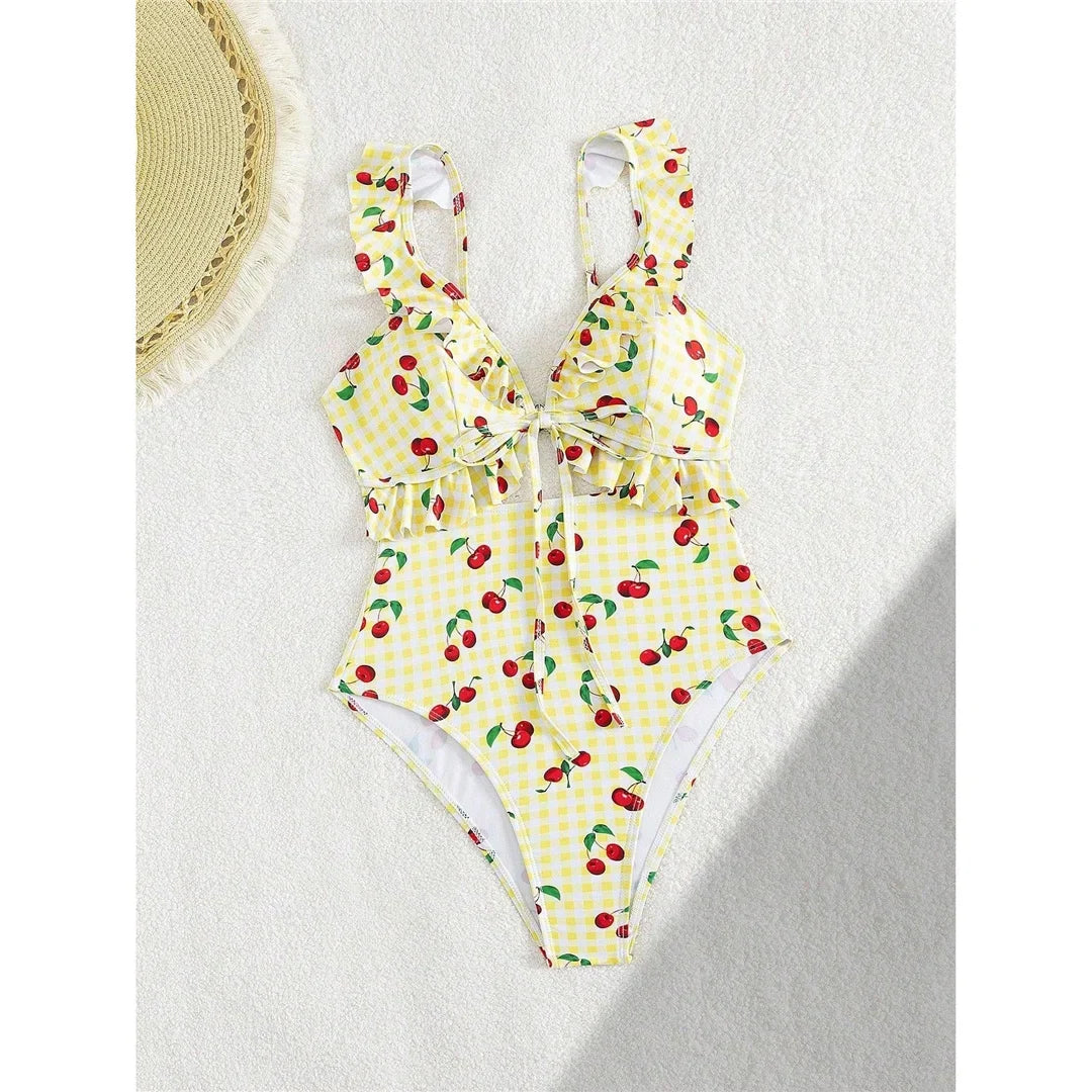 Maillot de bain une pièce échancré jaune clair à cerises posé à plat sur fond blanc, volants aux épaules et découpe en V