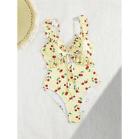 Maillot de bain une pièce échancré jaune clair à cerises posé à plat sur fond blanc, volants aux épaules et découpe en V