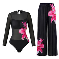 Maillot une pièce noir en mesh à manches longues et grande fleur rose sur le côté, posé avec son pantalon sur fond blanc