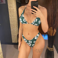 Bikini brésilien imprimé fleuri vert et blanc porté de face devant un miroir, fleurs blanches sur fond vert foncé