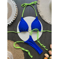 Bikini string tour de cou échancré à empiècements bleu roi posé à plat sur un tapis rond en corde et des sets en paille