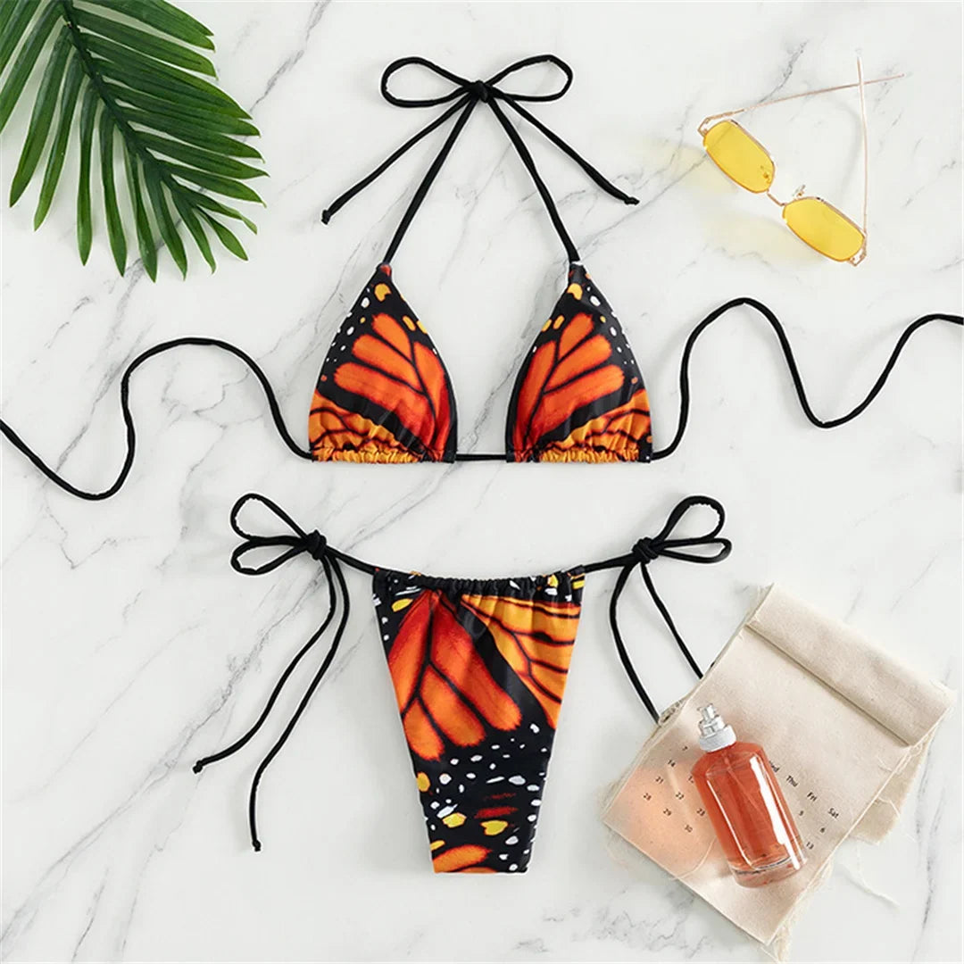 Maillot de bain deux pièces tour de cou imprimé rouge à ailes de papillon posé à plat sur marbre, haut triangle et bas à liens noirs