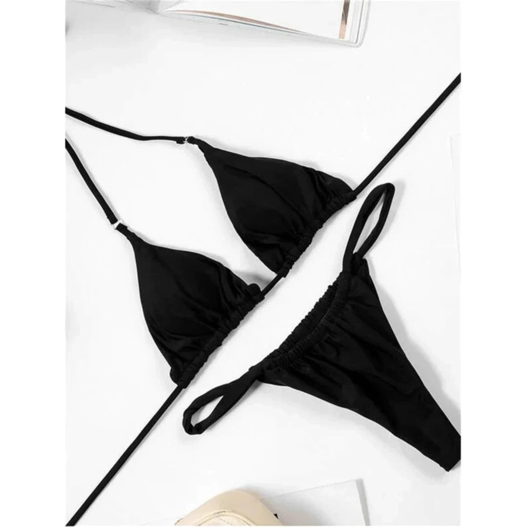 Bikini string triangle froncé noir posé à plat sur un fond blanc, bretelles fines et bas froncé
