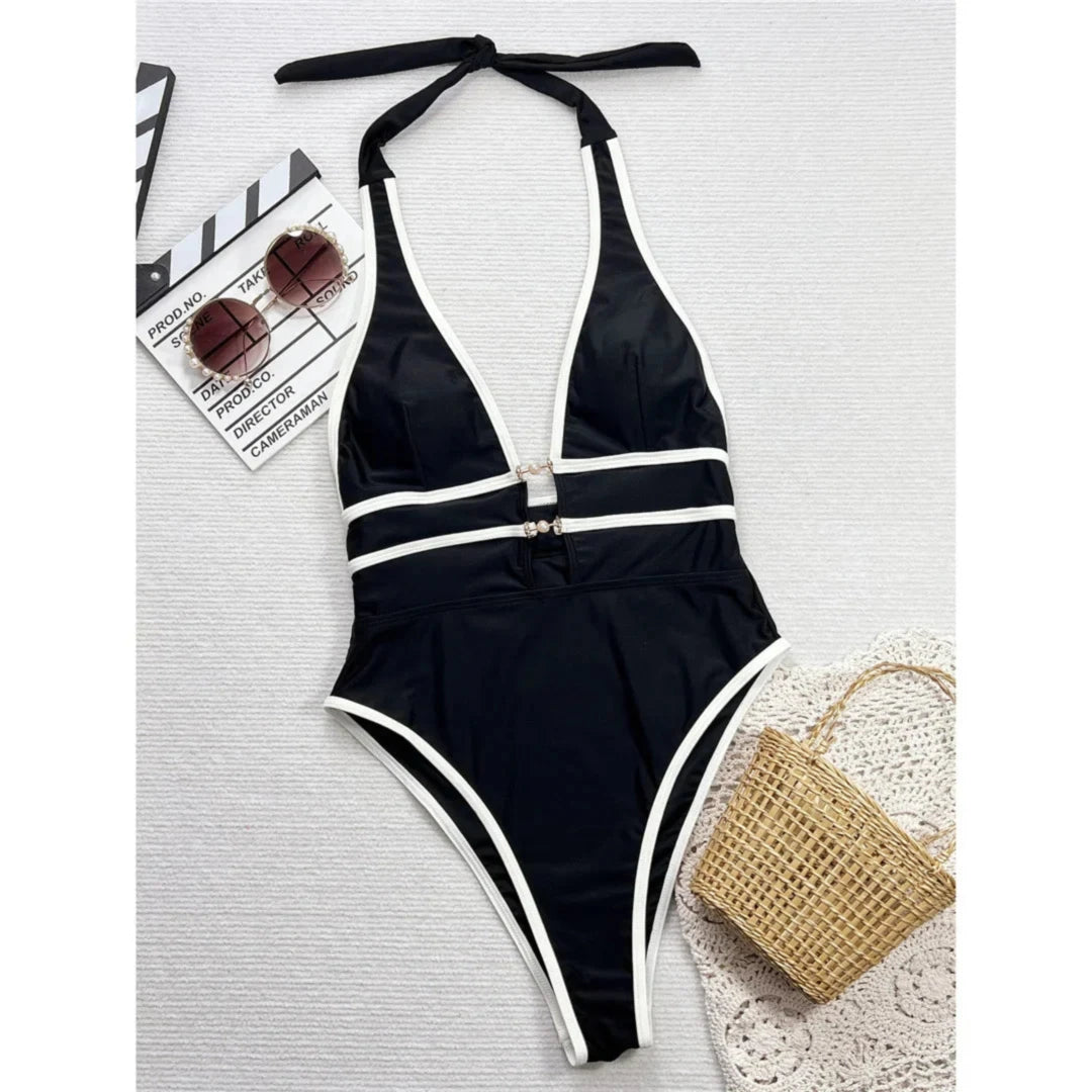 Maillot de bain une pièce tour de cou noir bordé de blanc posé à plat avec des lunettes de soleil et un sac tressé