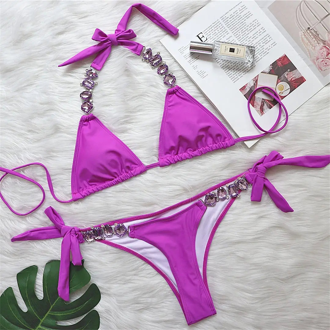 Bikini brésilien à strass effet diamant brillant violet à plat sur une fourrure blanche, à côté d'un magazine