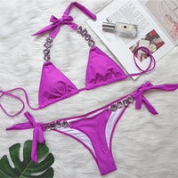 Bikini brésilien à strass effet diamant brillant violet à plat sur une fourrure blanche, à côté d'un magazine