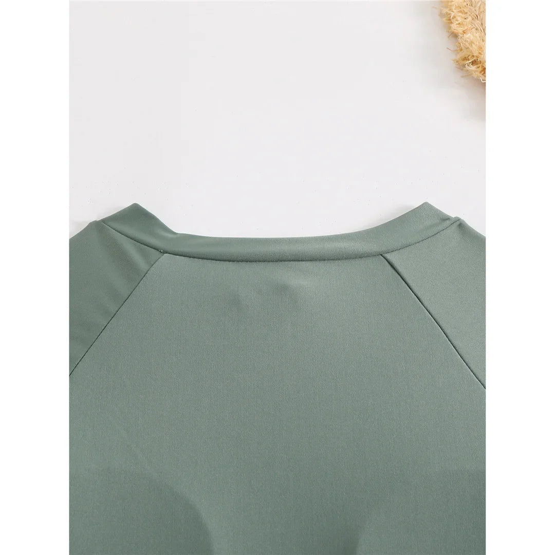 Gros plan sur l’épaule du maillot vert foncé à manche longue et couture raglan, sur un fond clair