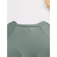 Gros plan sur l’épaule du maillot vert foncé à manche longue et couture raglan, sur un fond clair